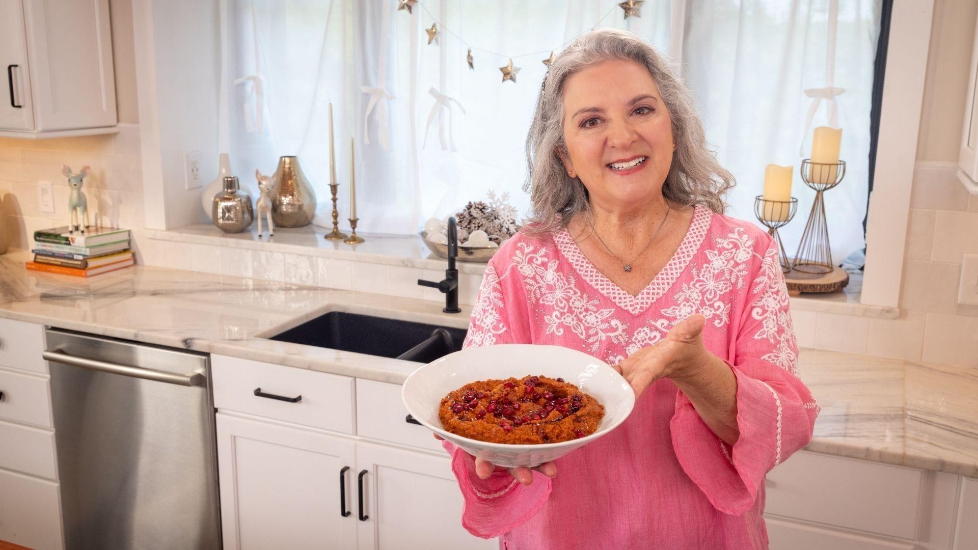 Sheri Castle holding up a dish of roasted red pepper and walnut dip.
