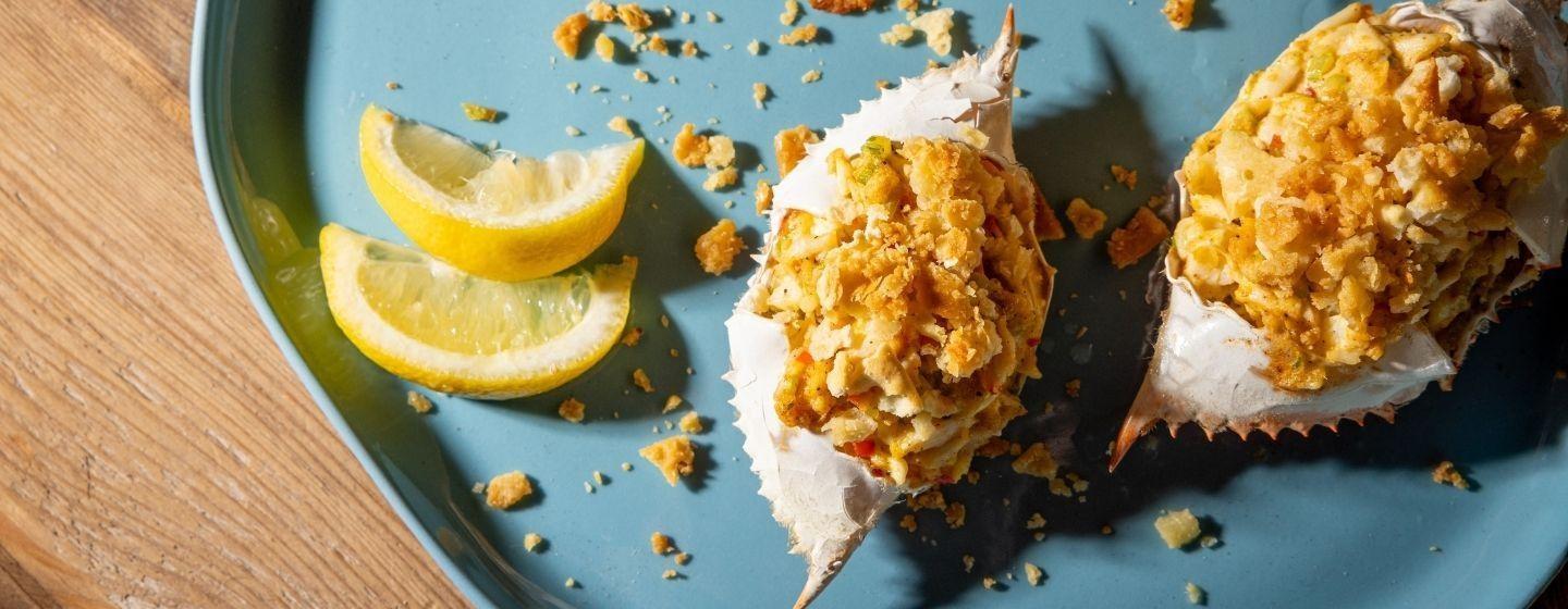 Deviled crab and lemons on a teal ceramic plate.