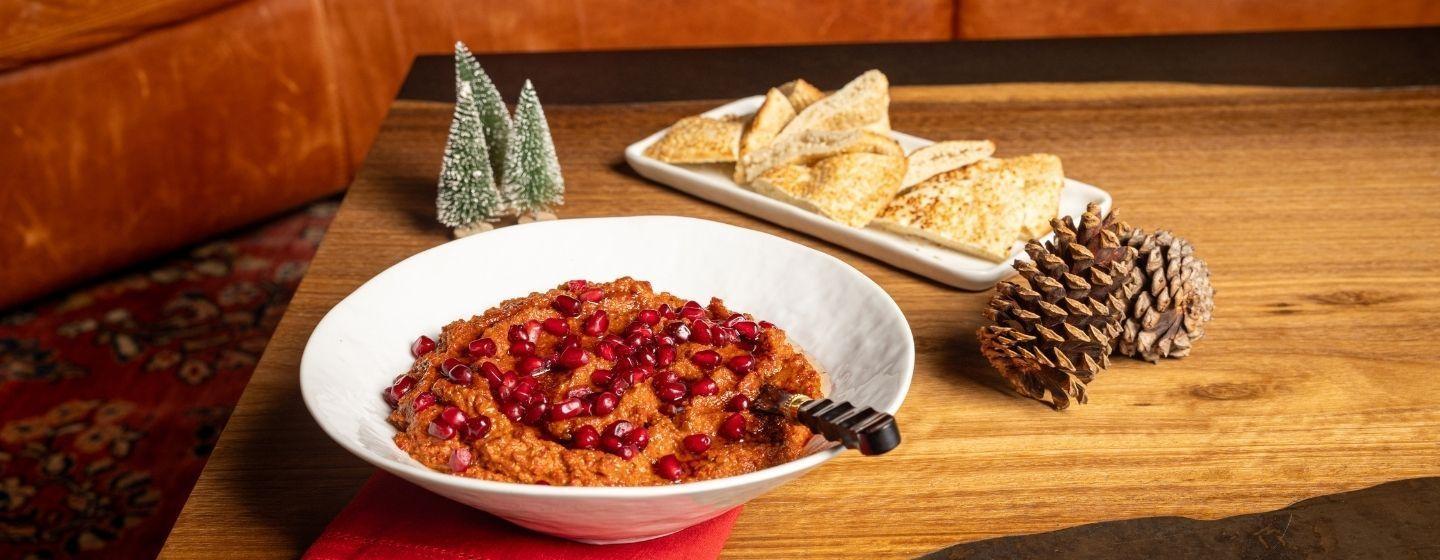 Roasted red pepper and walnut dip in a white ceramic dish with pomegranate seeds sprinkled on top.