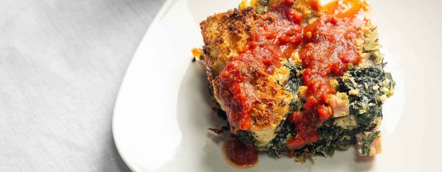 Savory ham, cheese and spinach bread pudding on a white ceramic plate.