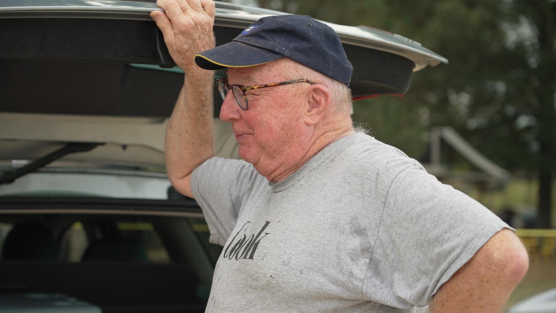 Bill Smith in a grey tee shirt and dark blue baseball cap standing behind Sheri Castle's car.