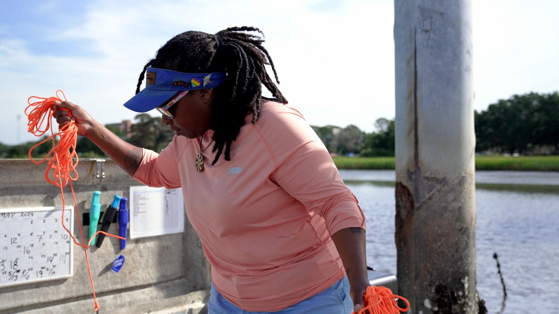 Tia Clark rounding up some orange fishing rope on a dock.