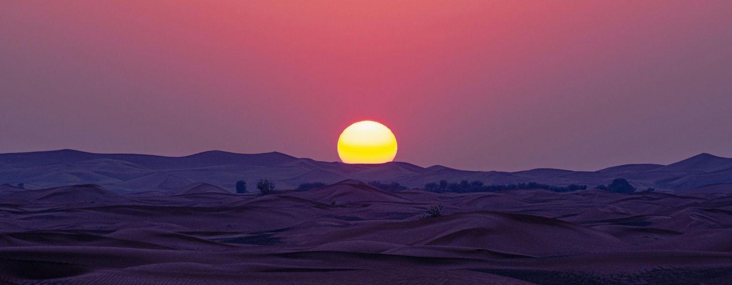 Sky at sunset that's orange, pink and purple over a mountain range.