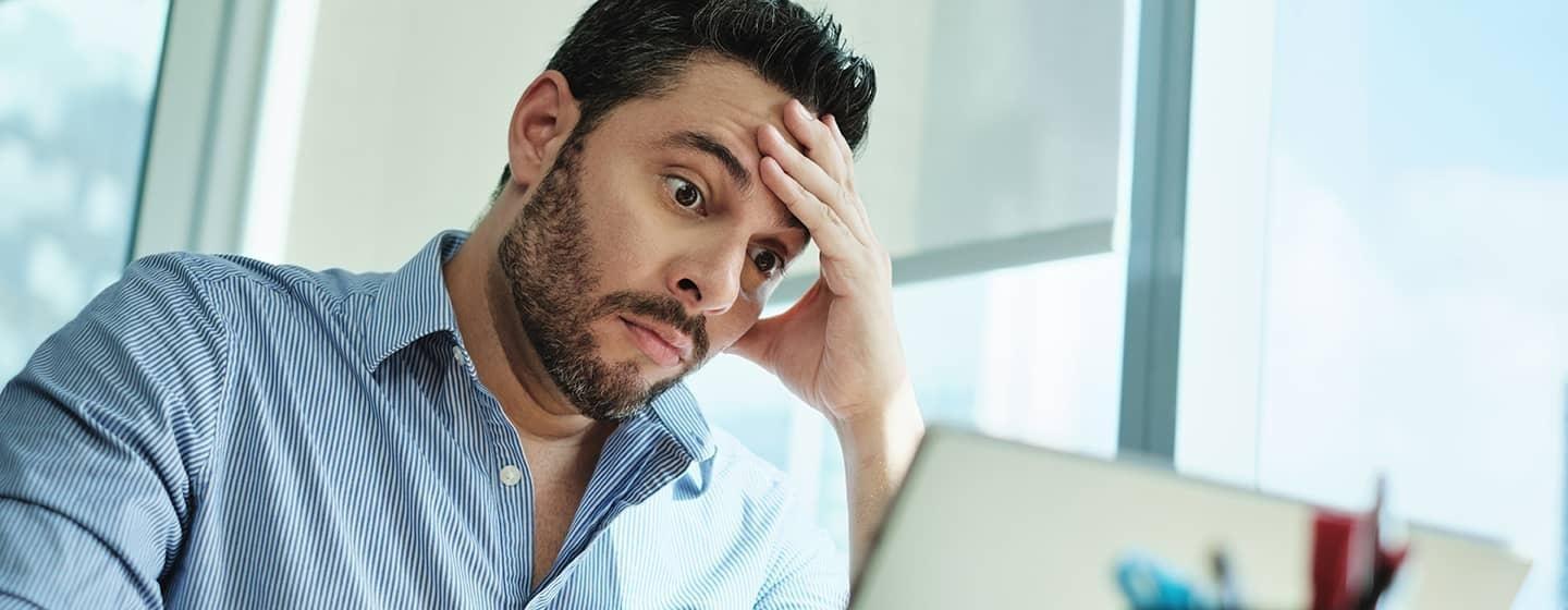 stressed man sitting at work computer hand on face