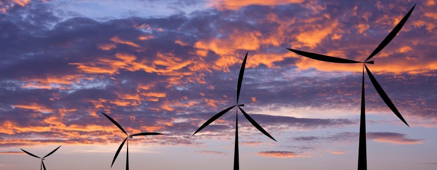 Four wind turbines in a row with a pink and purple, cloudy sunset in the background.