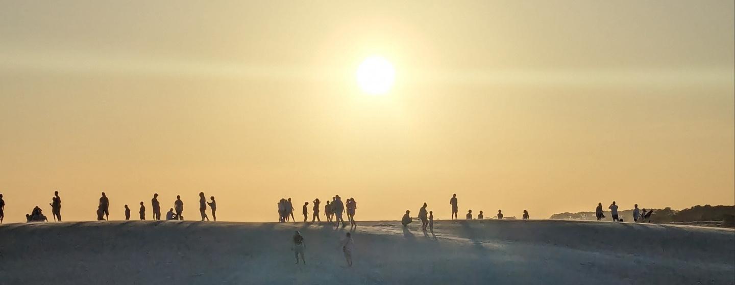 Several people standing on a ridge with the sun setting in the background.
