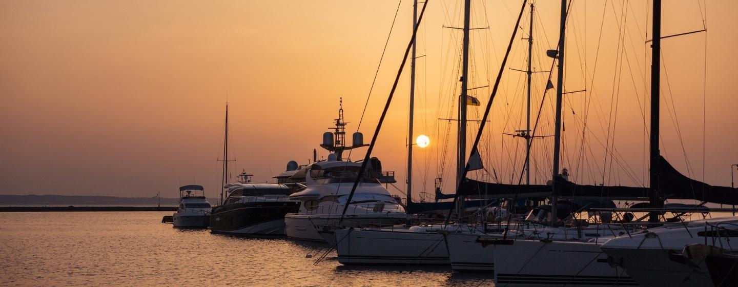 A pier with a line of sail boats with a peachy sunset on the horizon.