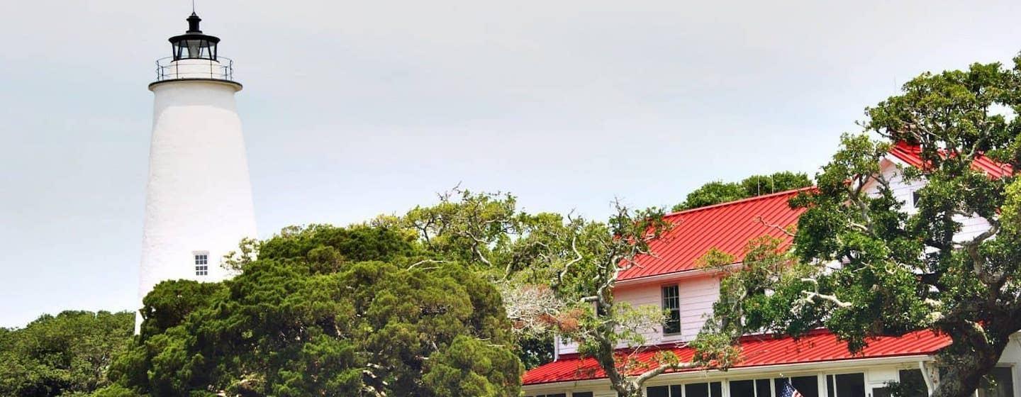 A lighthouse stands behind a foreground of trees and a red-roofed house
