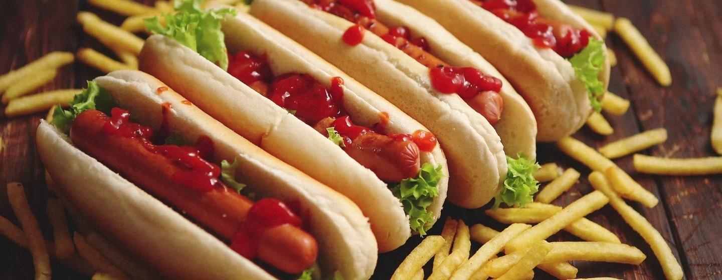 Four hotdogs with ketchup on them surrounded by fries.