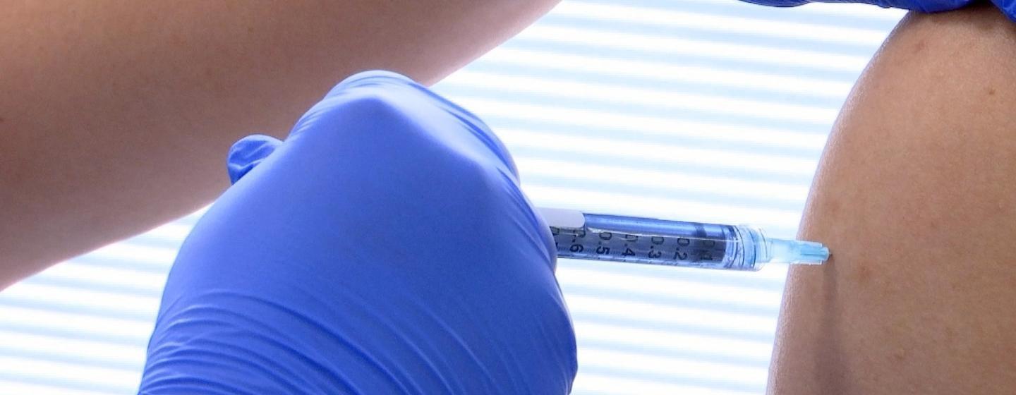 Gloved hands using a syringe to inject a shot into another person's shoulders.