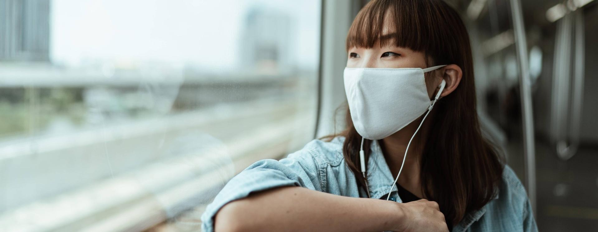 masked woman looking out window of train