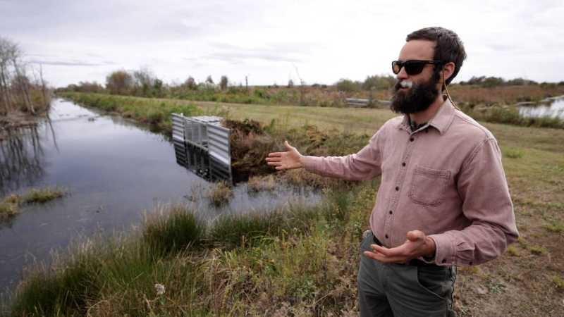 A man gestures towards a silver corrugated metal structure in the corner where two canals meet.