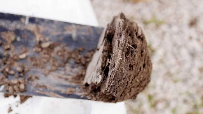 A narrow shovel fills the frame with a scoop of soil on it that is brown with lighter brown, almost white layers. The layers are thin and almost look flaky.