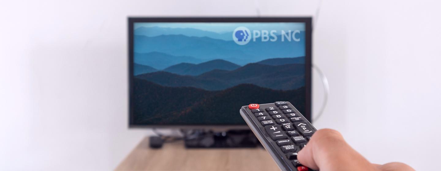 A hand holding a remote that's being pointed to a TV with the Blue Ridge Mountains on it.