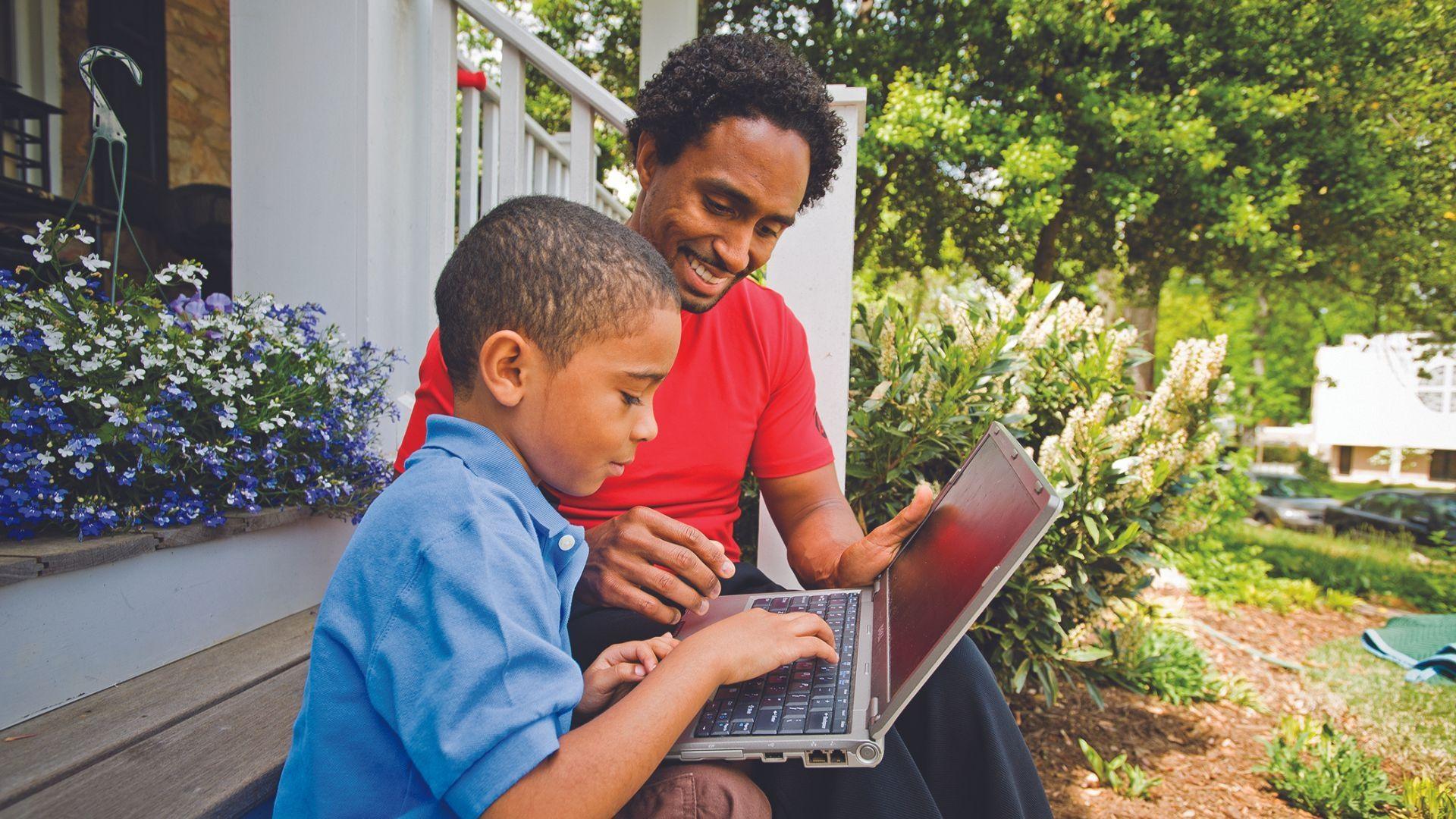 Father and son on home steps with laptop.