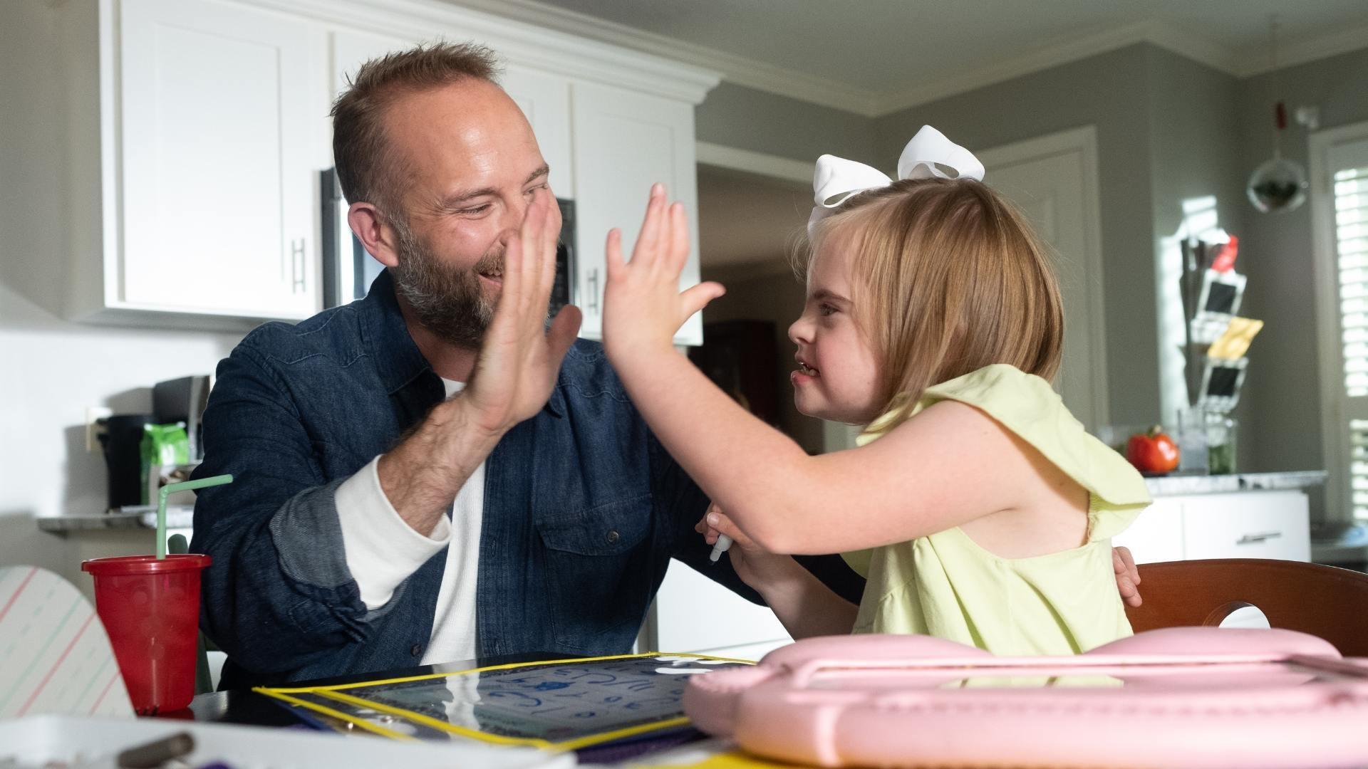 Father high fives daughter at the kitchen table.