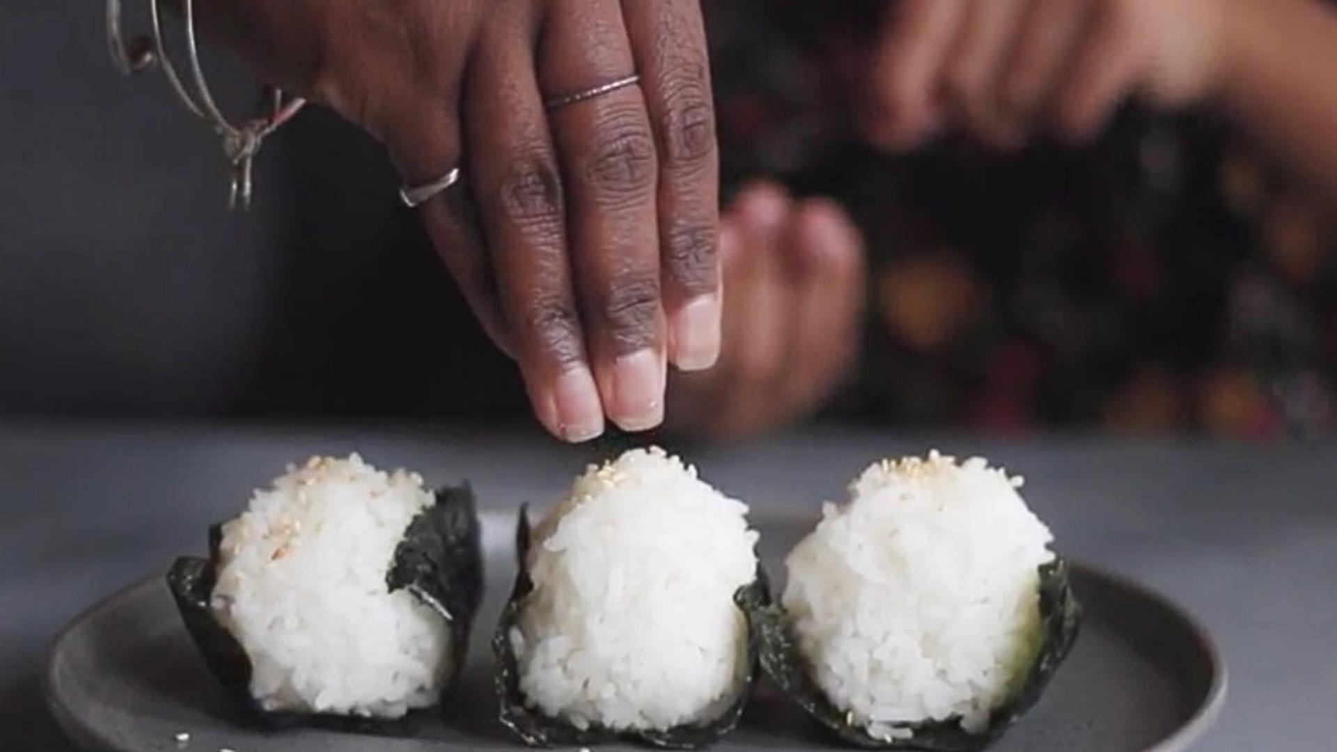 A hand pinched above three onigiri rice balls.