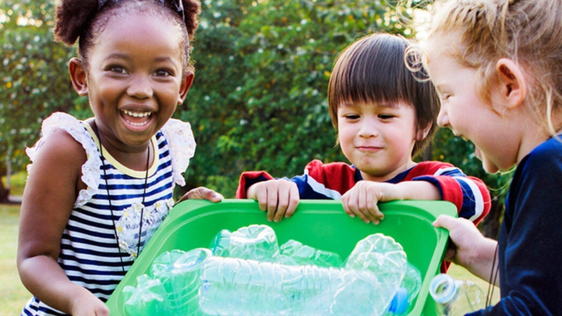 Three children collecting plastic bottles in a green bin.