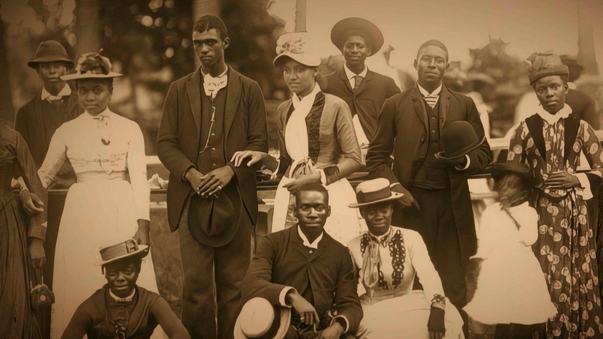 A sepia-toned image of a group of Black people in hats, dresses and suits. 