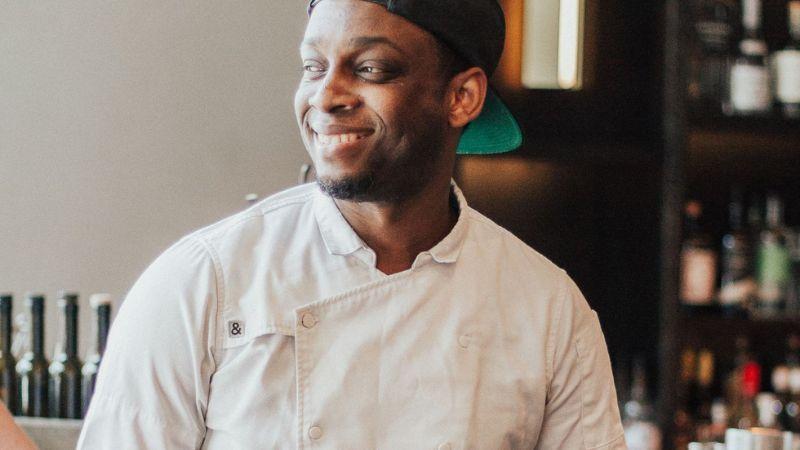 Cleophus Hethington wearing a chef's coat and backwards cap and smiling in his kitchen