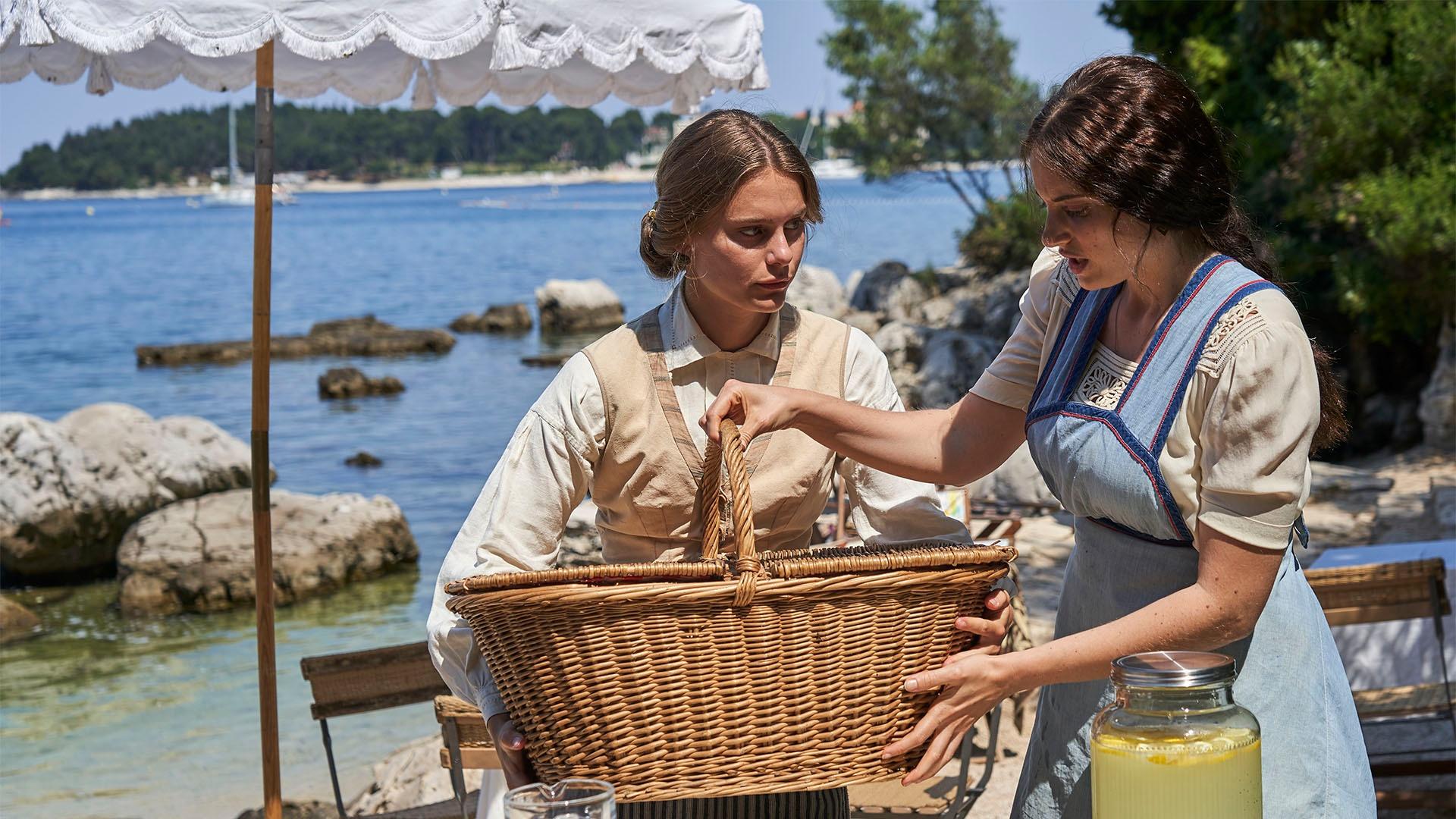 Constance (Louisa Binder) and Paola (Carolina Gonnelli) prepare a beach picnic. 