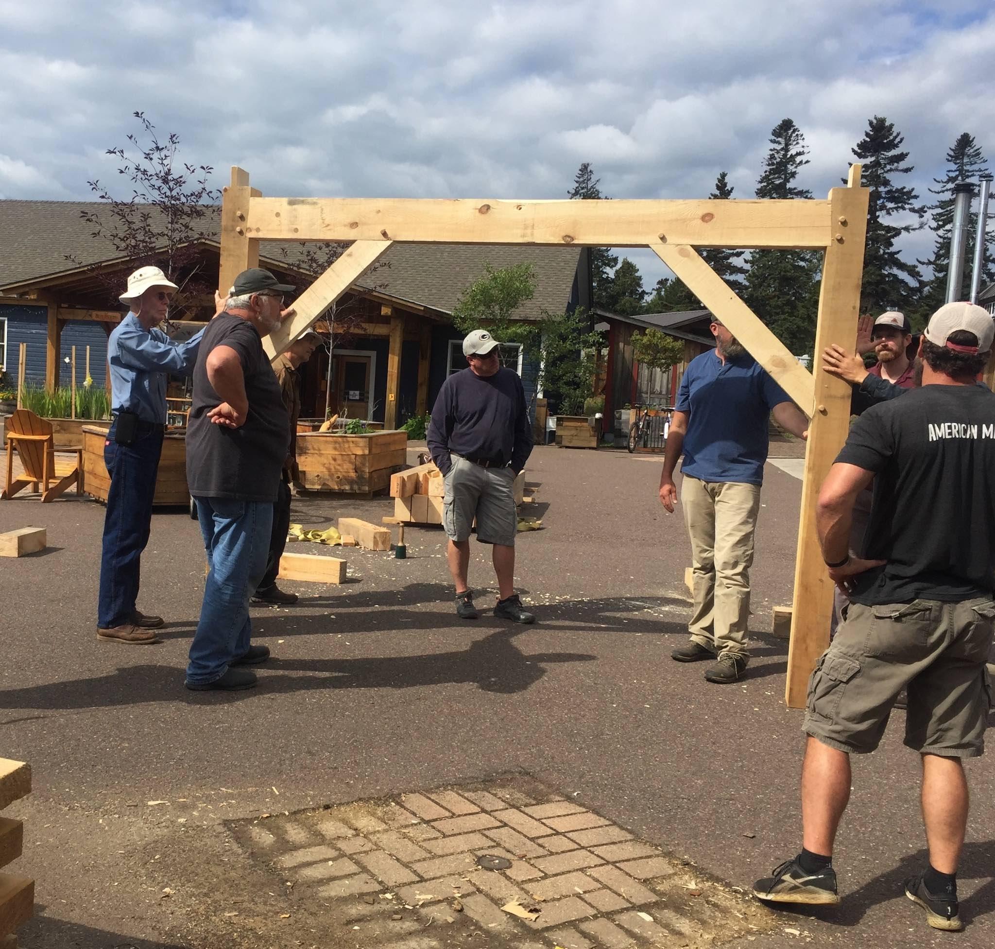 Students at North House Folk School's timber framing class hold up a timber frame