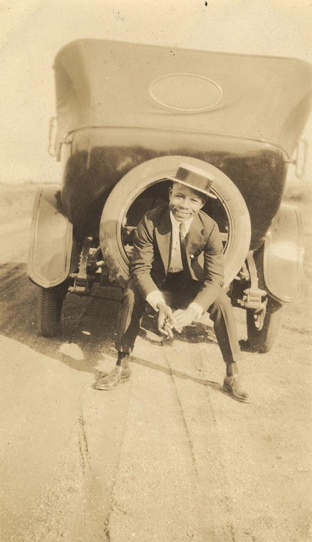 Young African American man sitting in the spare tire on the back of an automobile.
