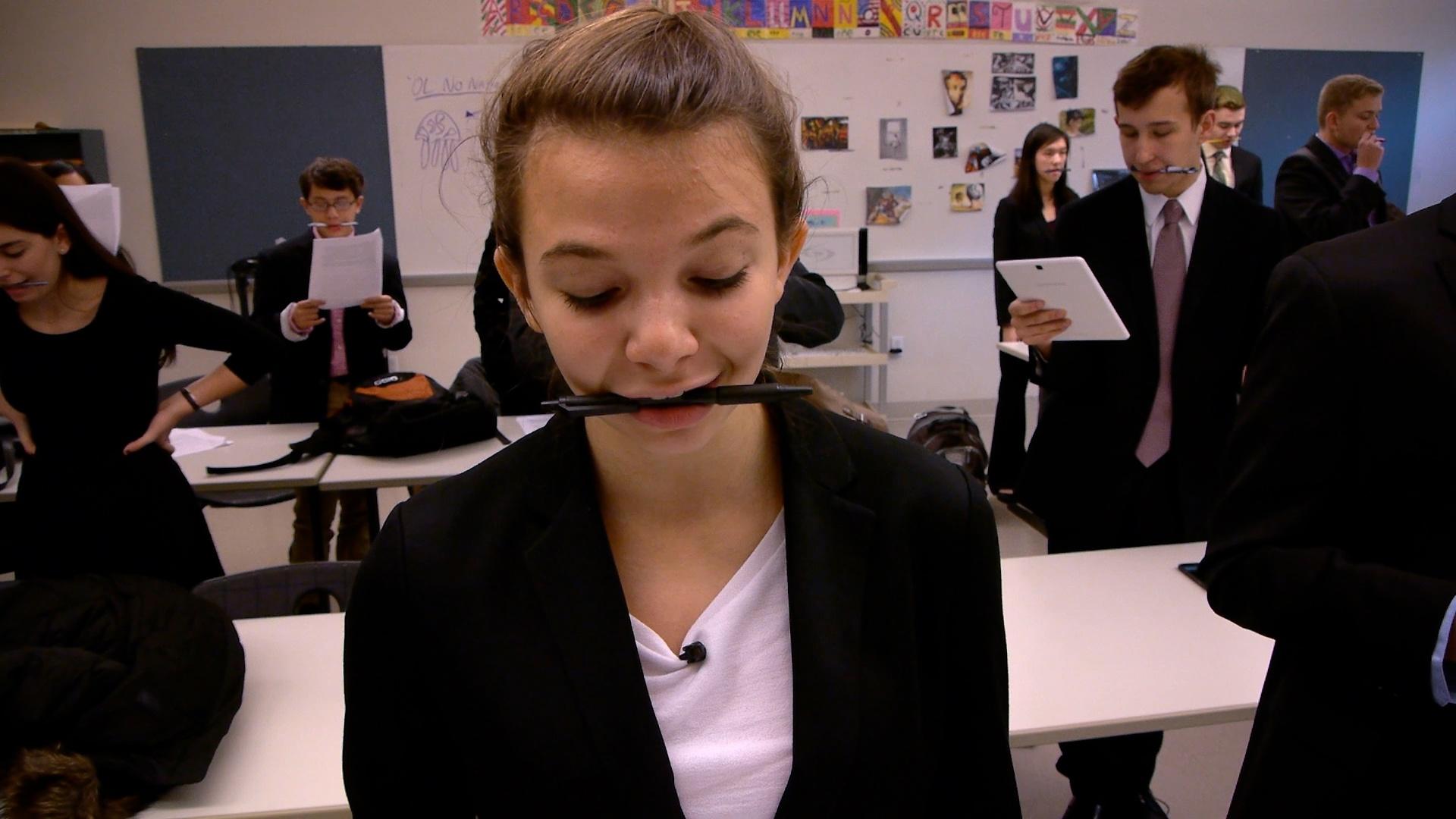 Gaby and fellow students participate in a speech exercise by talking with pens in their mouths.