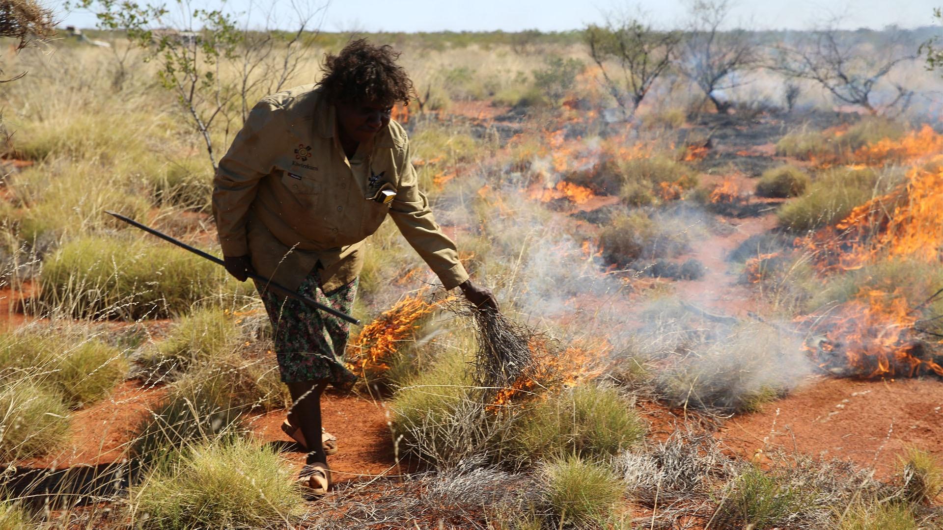 Image of a Kiwirrkurra Ranger setting controlled fires to the landscape in Australia.