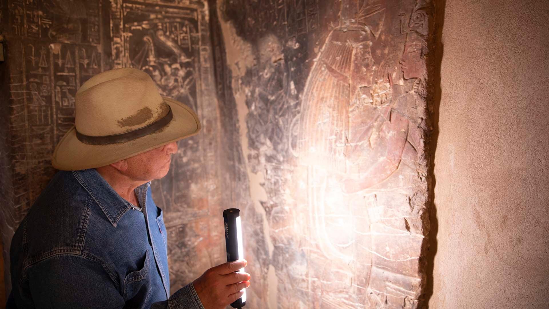 Image of a man holding a light to a relief in Maya's Tomb in Saqqara.