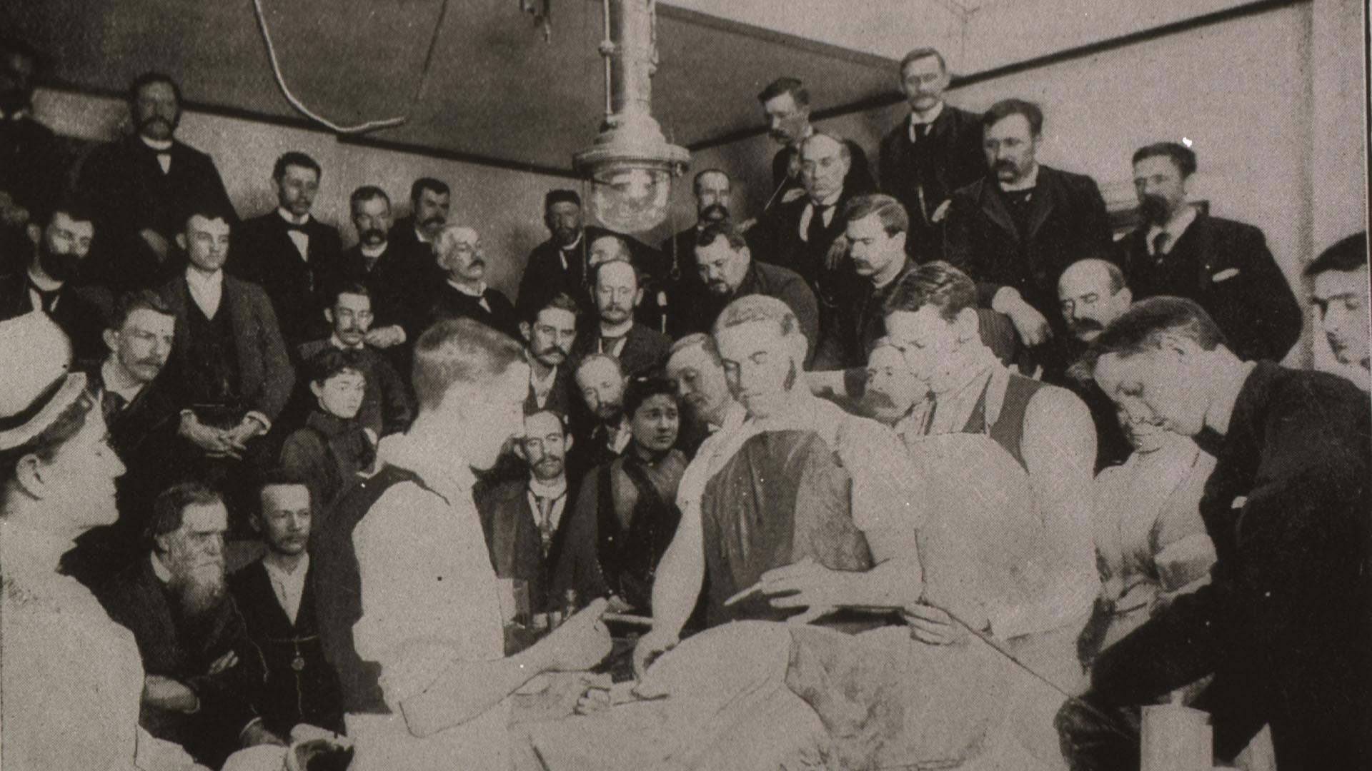 Two women observing an operation among a class of men in an Upper Operating Room.