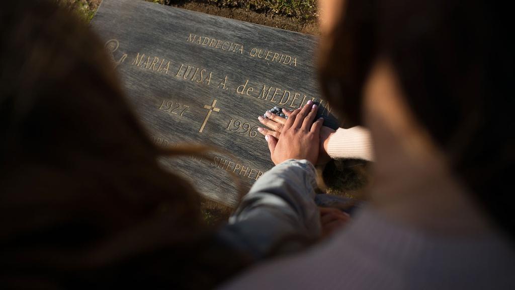 Sisters Alejandra Campoverdi and Monica Medellin place rosary beads on grandmother's gravesite.