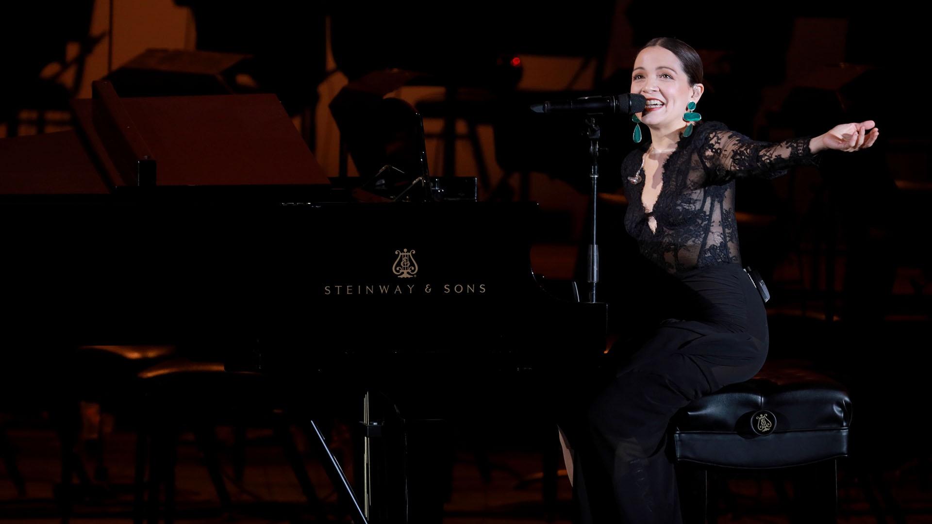 Natalia Lafourcade in black seated at the piano. 