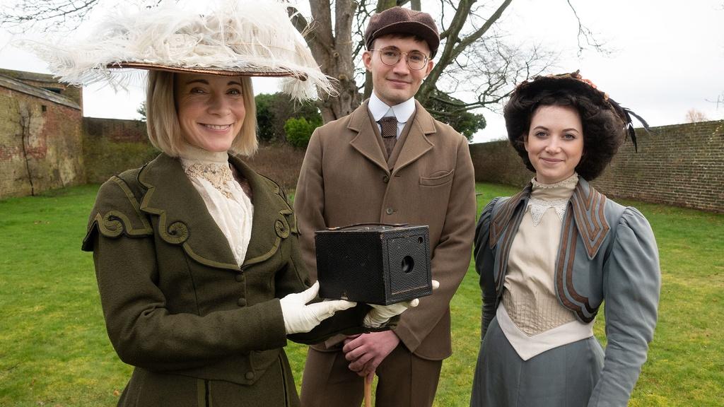Lucy Worsley in period costume, with extras and a vintage Kodak camera.