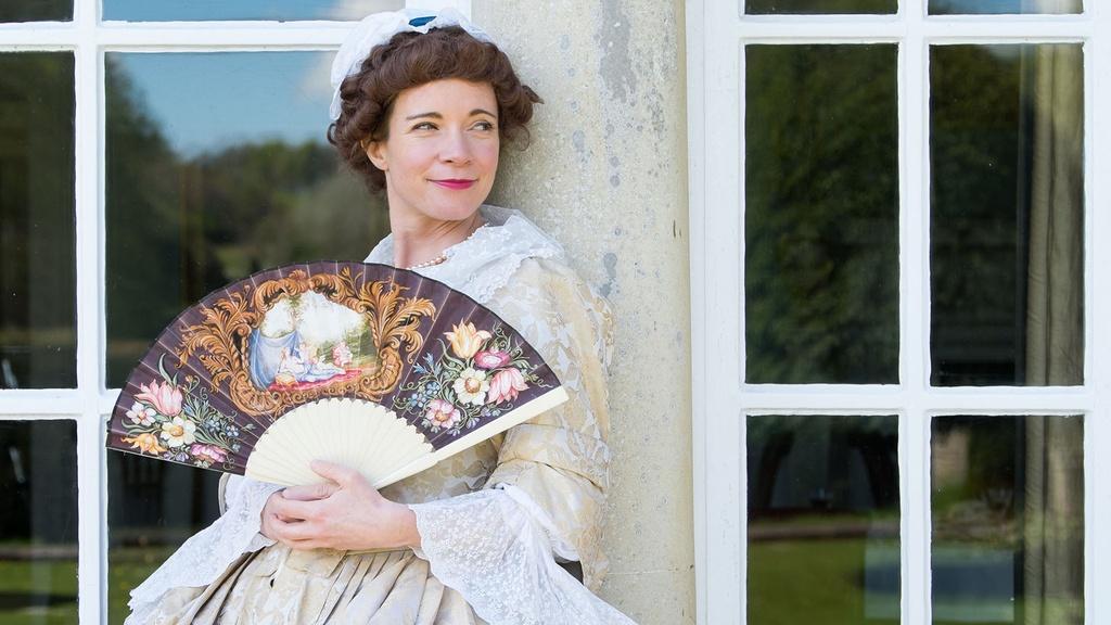 Lucy Worsley in Georgian Costume, holding a fan.