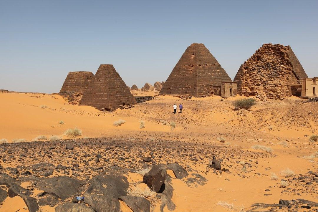 Meroitic Pyramids loom overhead as Henry Louis Gates, Jr. and Mahmoud Bashir walk closer to the ruins.
