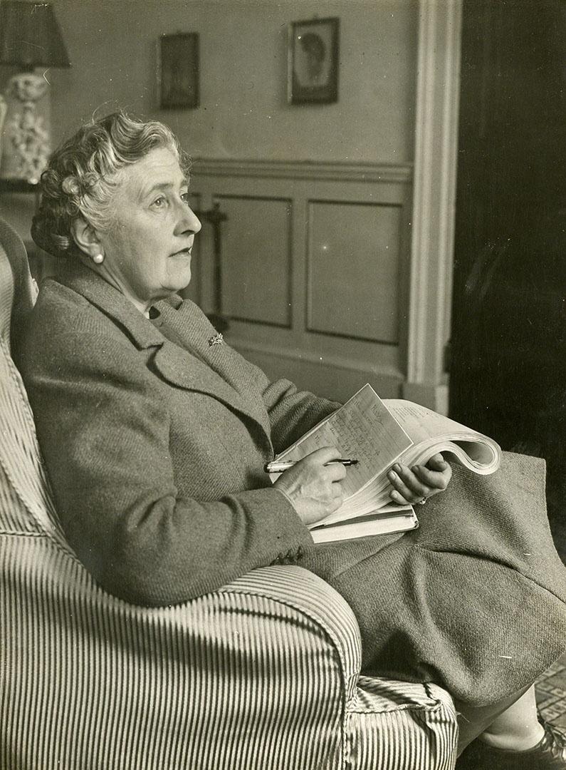 Agatha Christie sitting in her armchair with a newspaper.