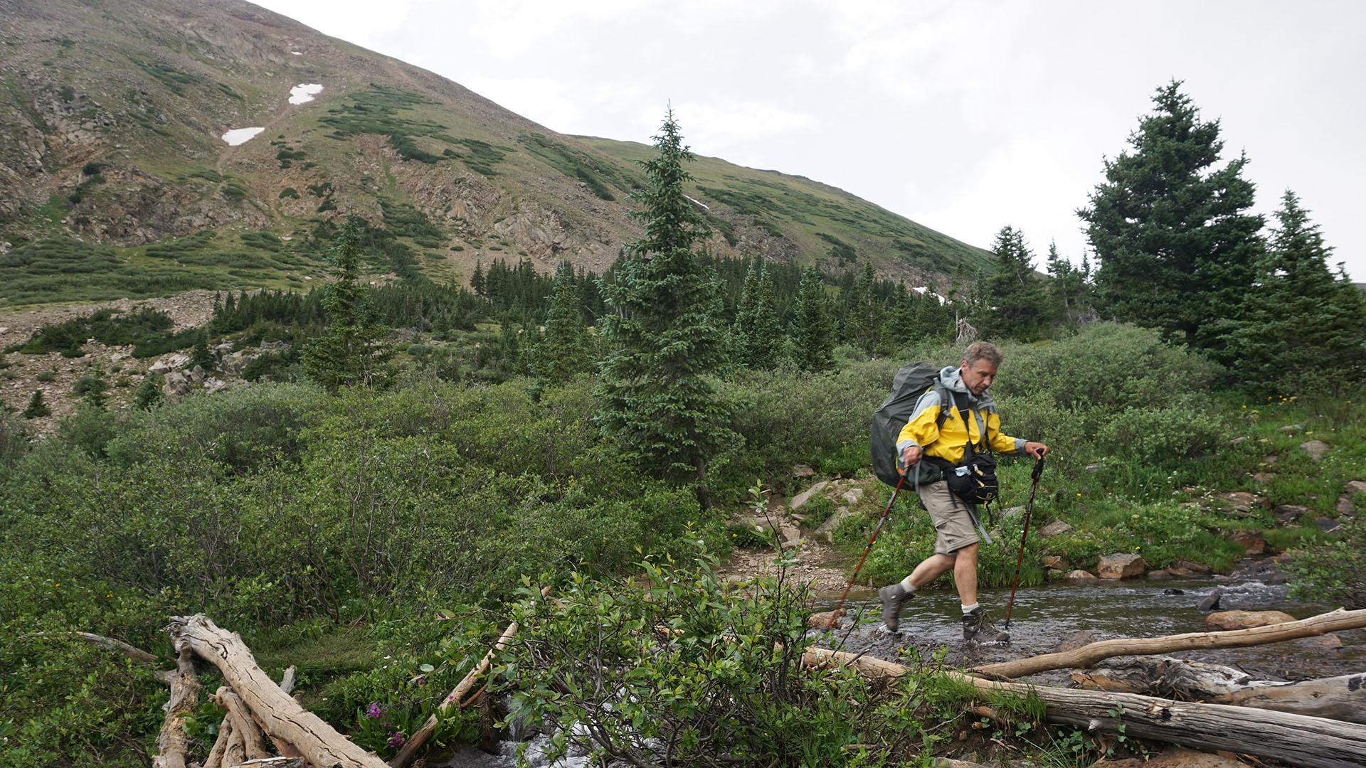 Mike Forsberg crosses a stream while hiking to follow the water.