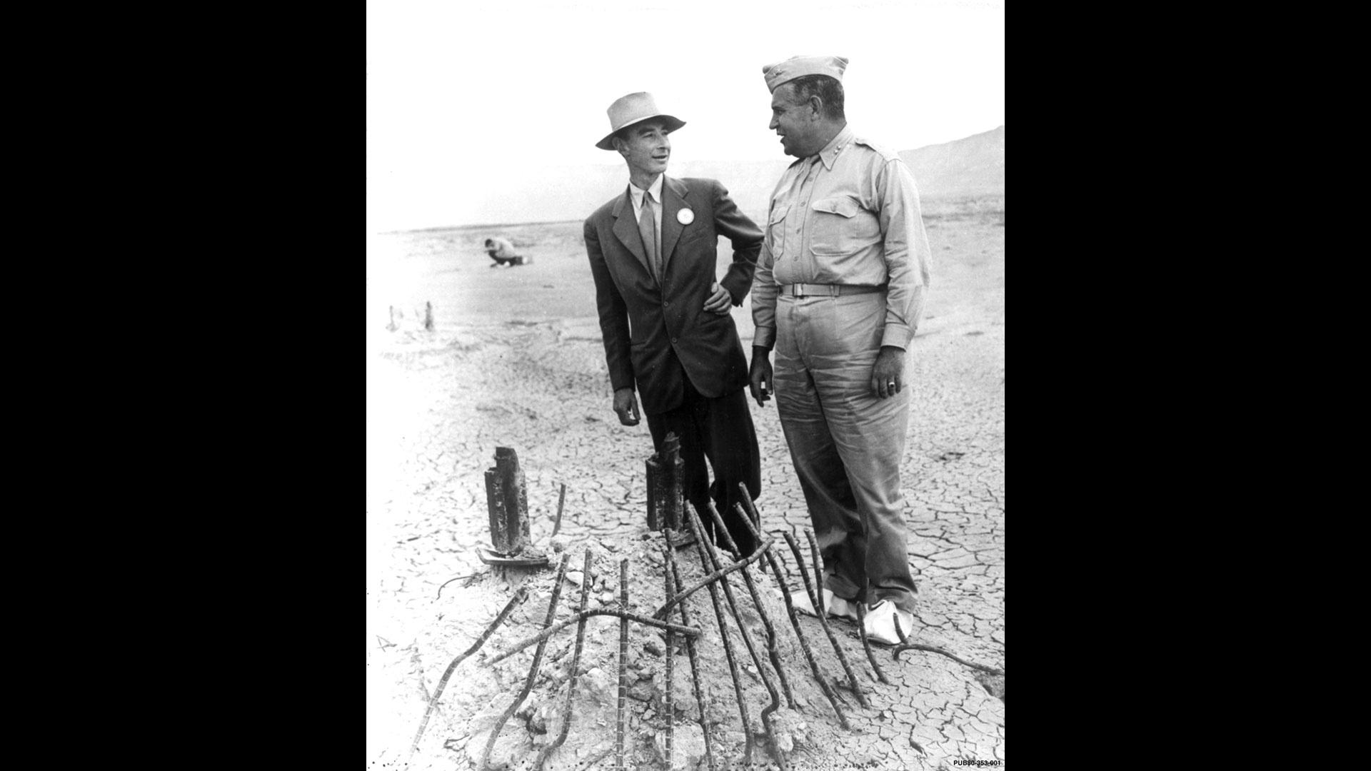 Groves and Oppenheimer stand around the Trinity bomb test site as they give the press a tour.