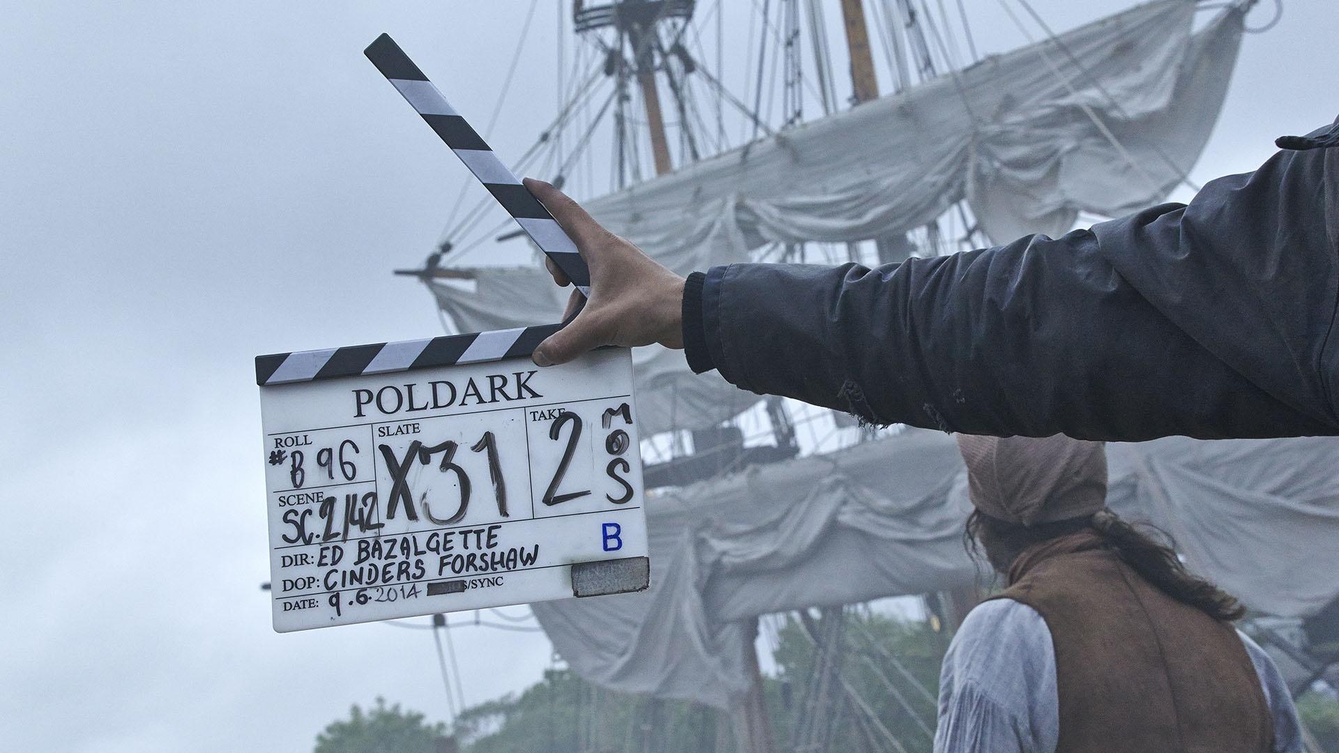 The Poldark clapperboard in front of tall ships.