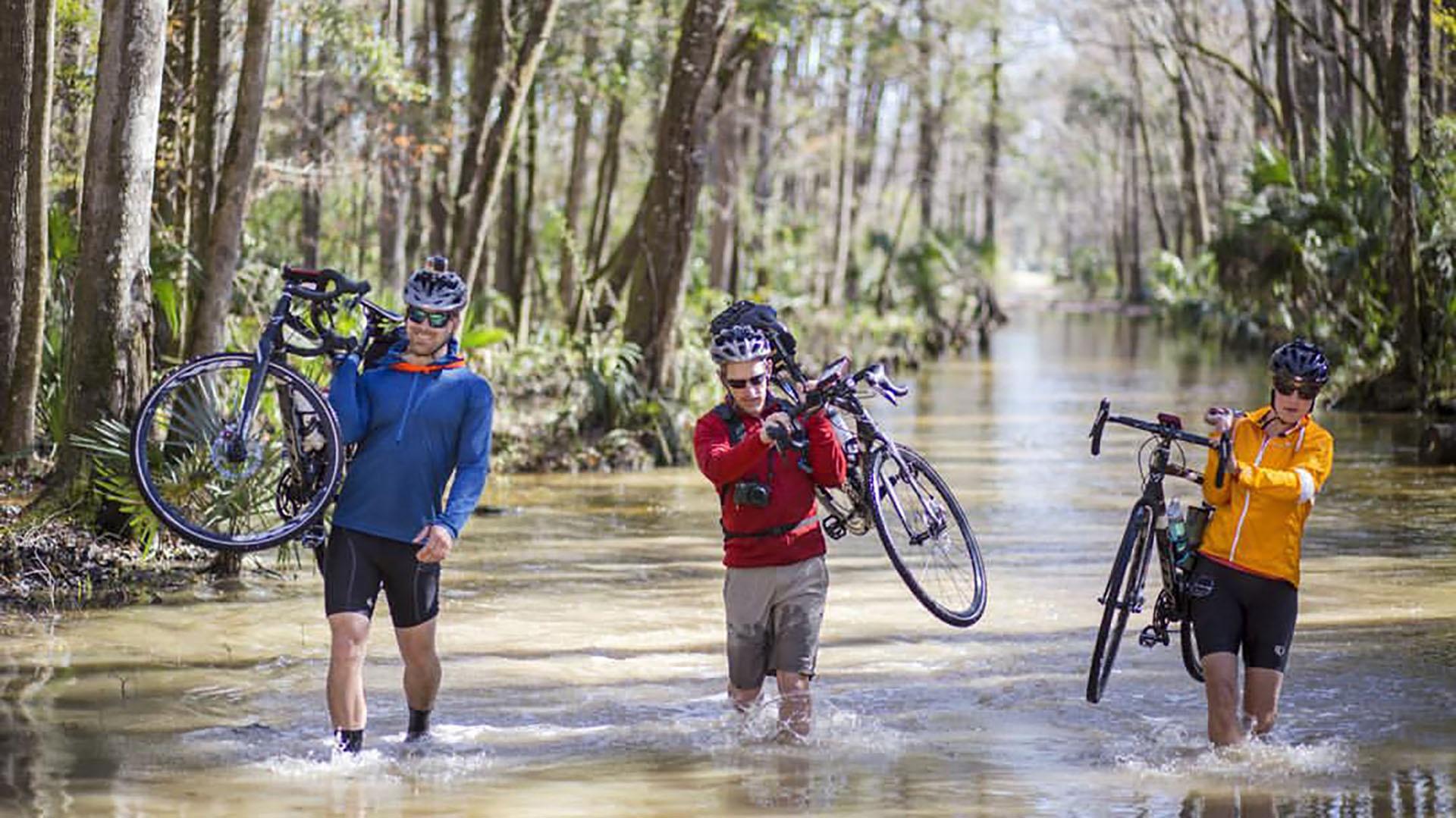 Joe Guthrie, Carlton Ward, and Mallory Dimmitt hoist their bikes across a deep crossing.
