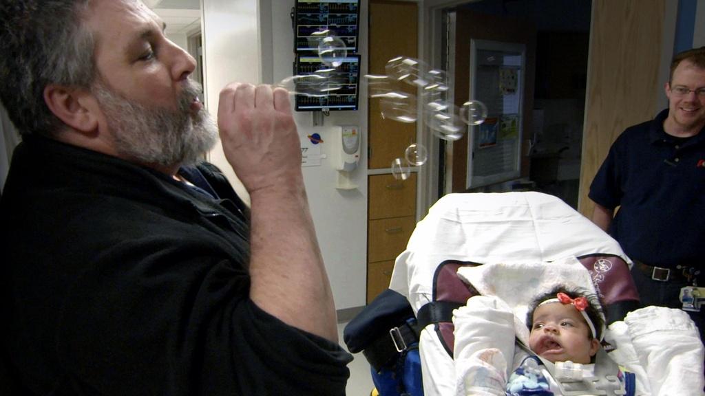 A member of the transport team blows bubbles to entertain Lilly.