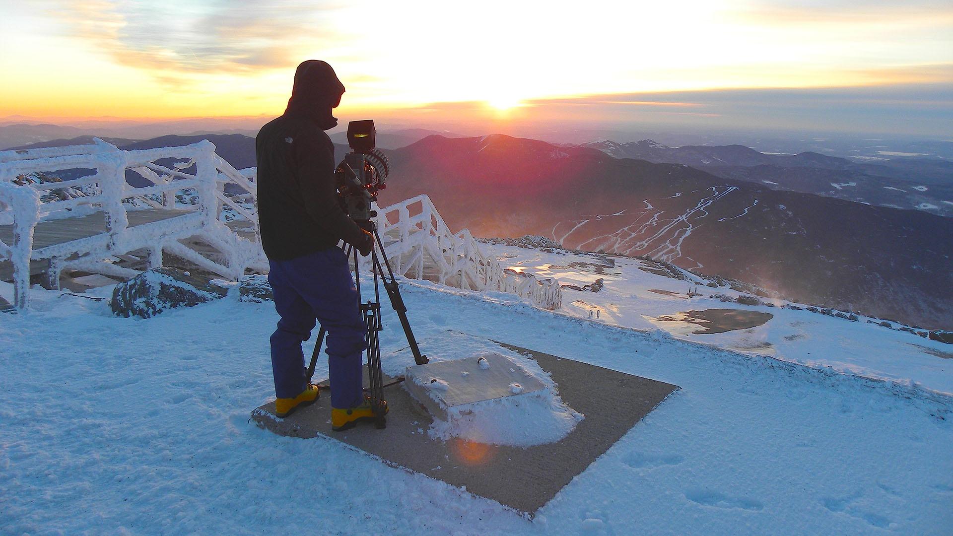 Cameraman filming sunrise on the summit of Mount Washington. NH, USA.