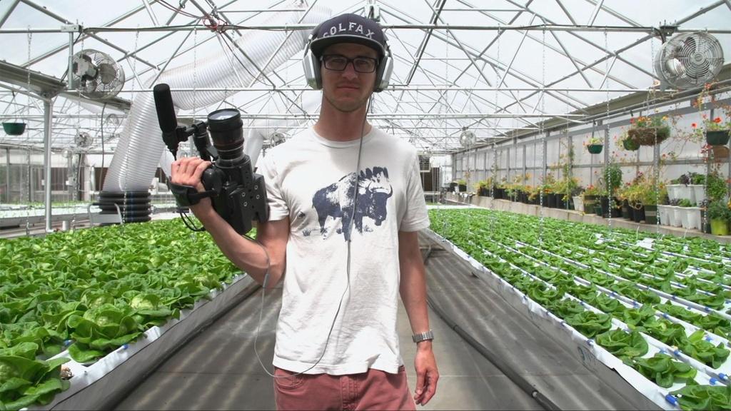 Image of man holding camera in greenhouse