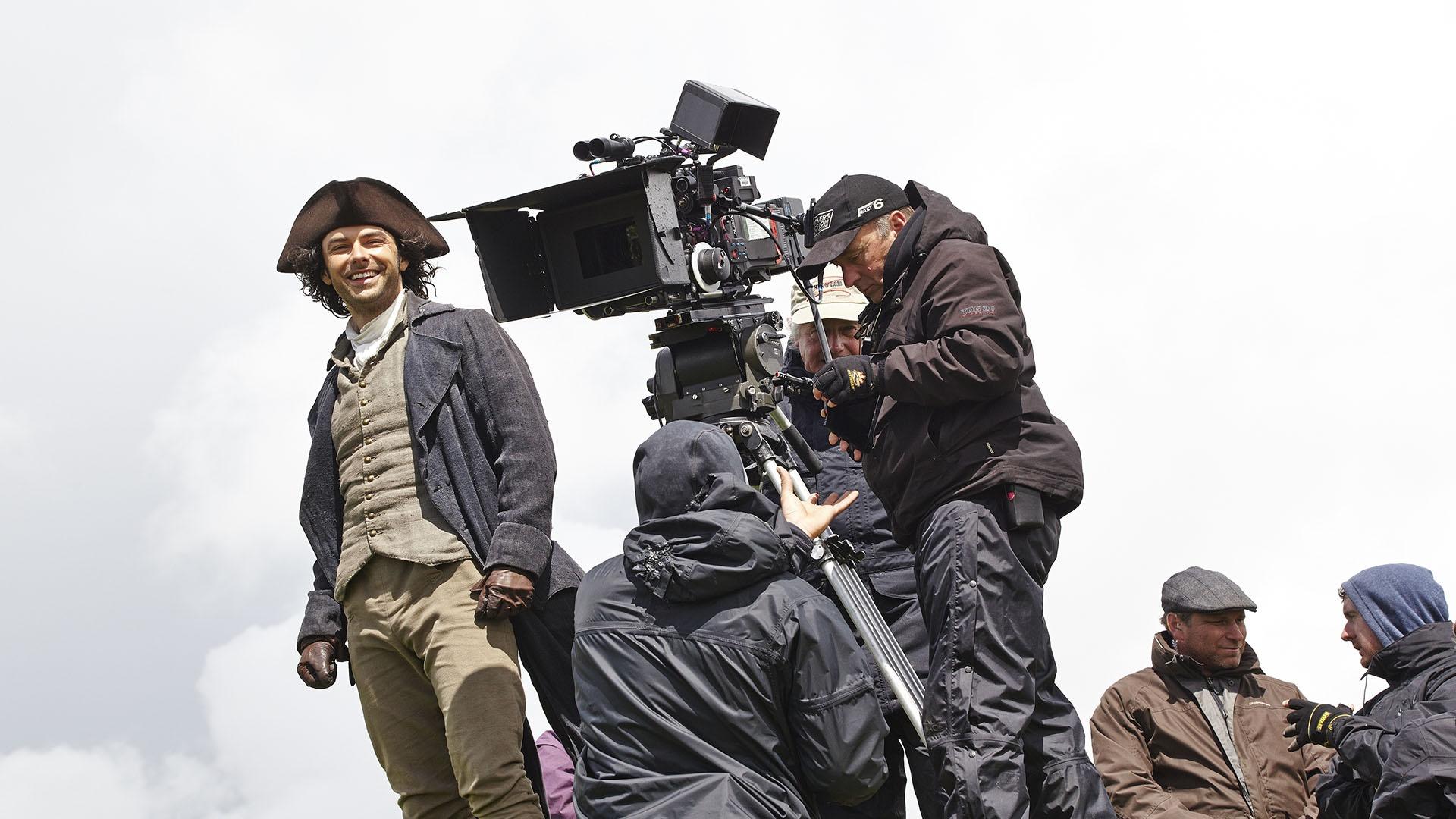 Aidan Turner, in costume as Ross Poldark, stands by the camera.
