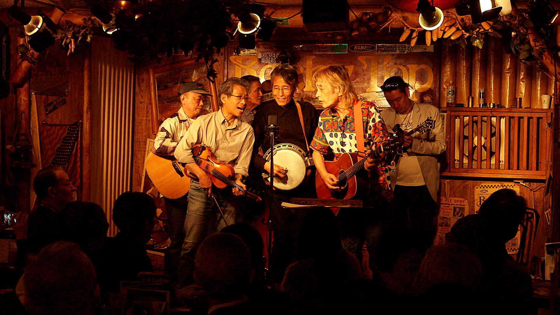 Still image of six musicians performing on stage.