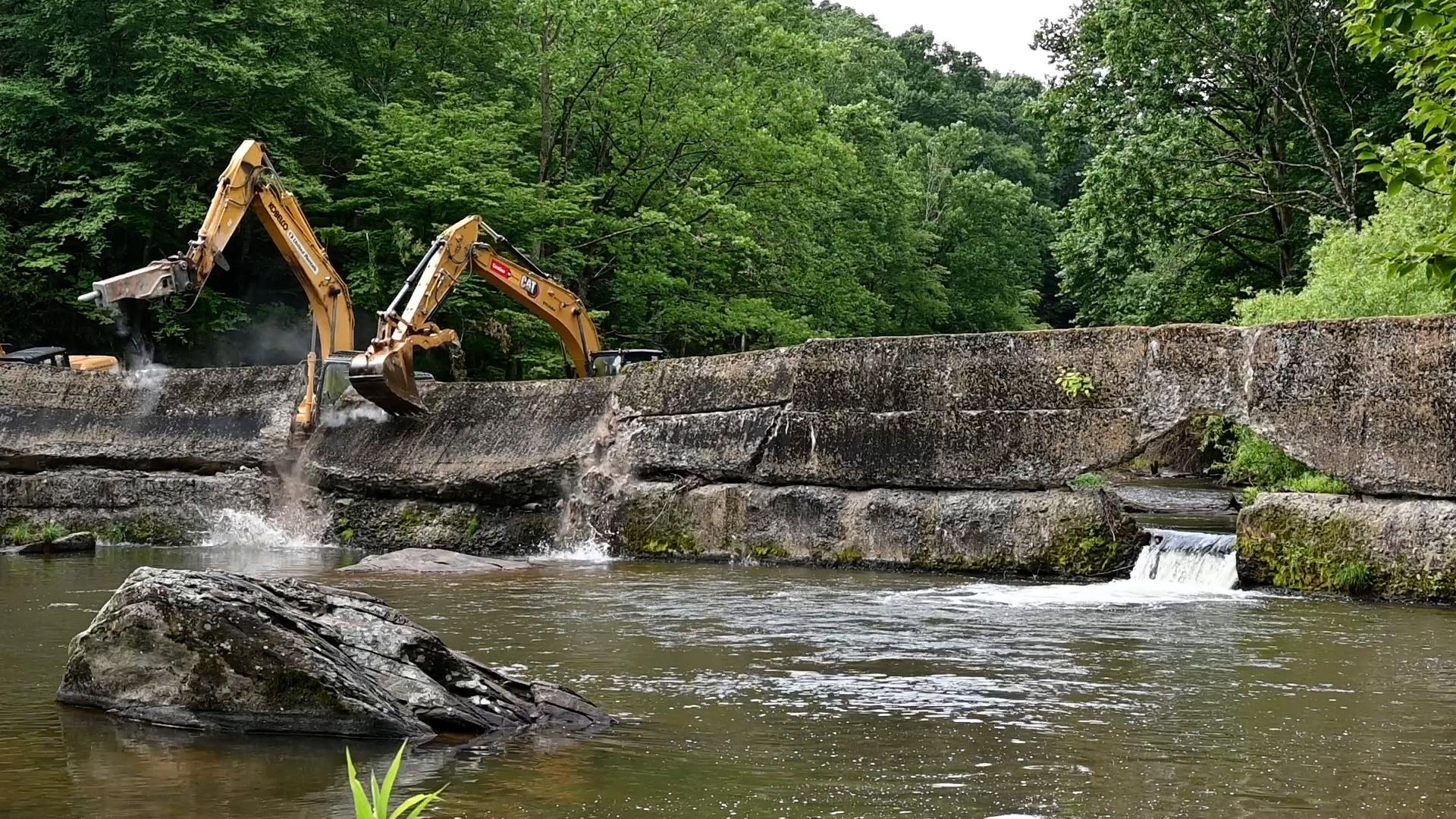 Two excavators tearing down a river dam.