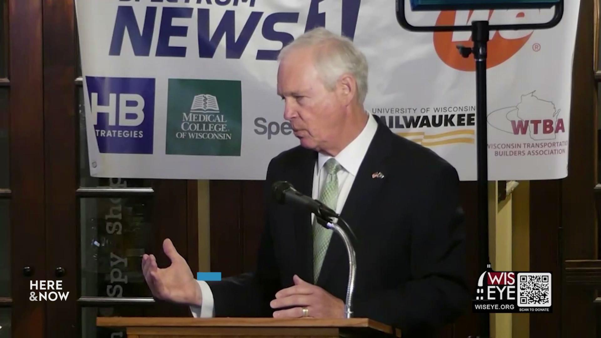 A still image shows U.S. Senator Ron Johnson speaking at a podium in front of a banner of associations he supports, including three that read 'Medical College of Wisconsin,' 'University of Wisconsin Milwaukee' and 'Wisconsin Transportation Builders Association.'
