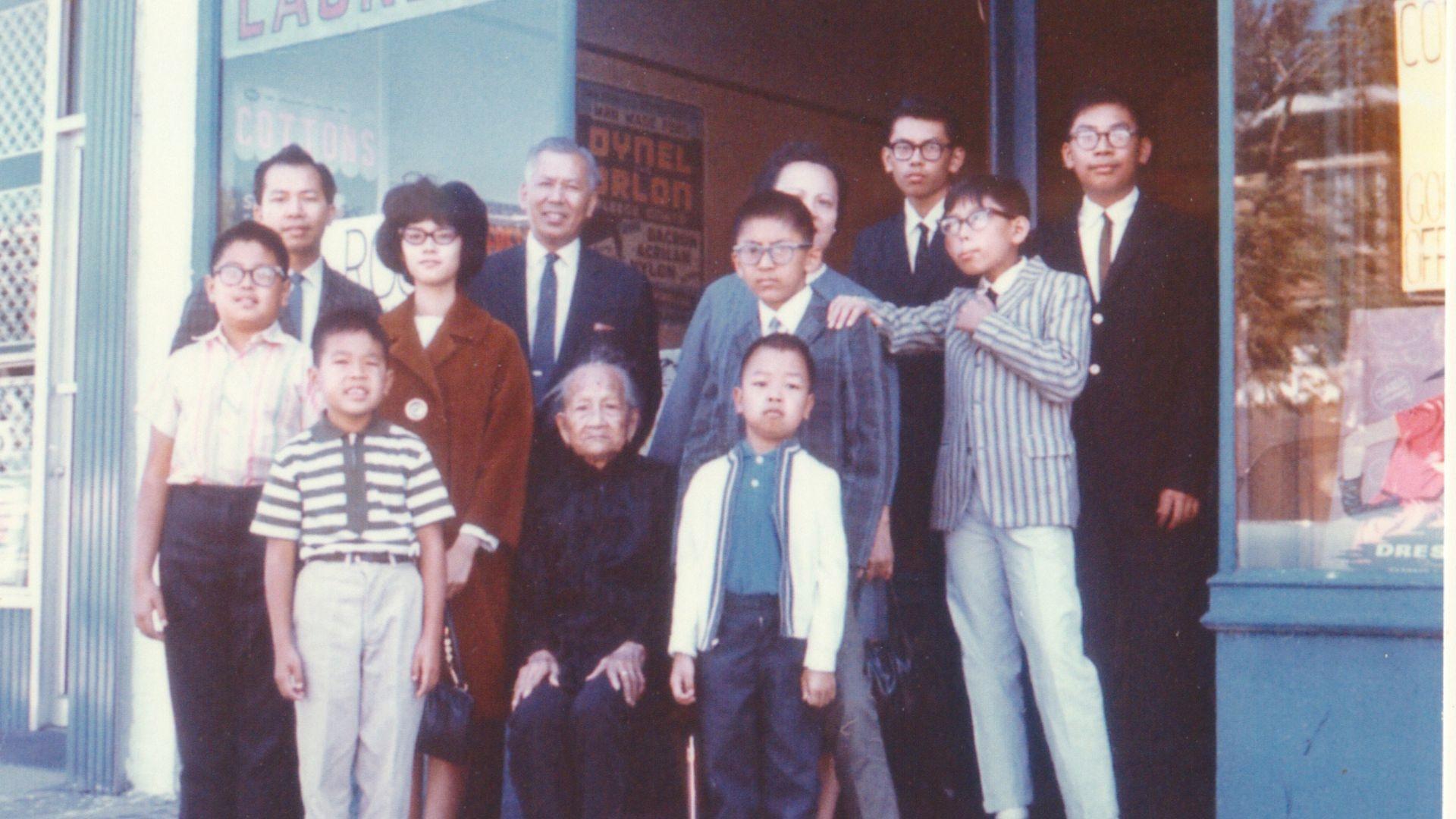 Corky Lee and his family gather for a portrait in front of their laundry in Queens, NY. (Lee is third from the right in suit and tie in back row.)