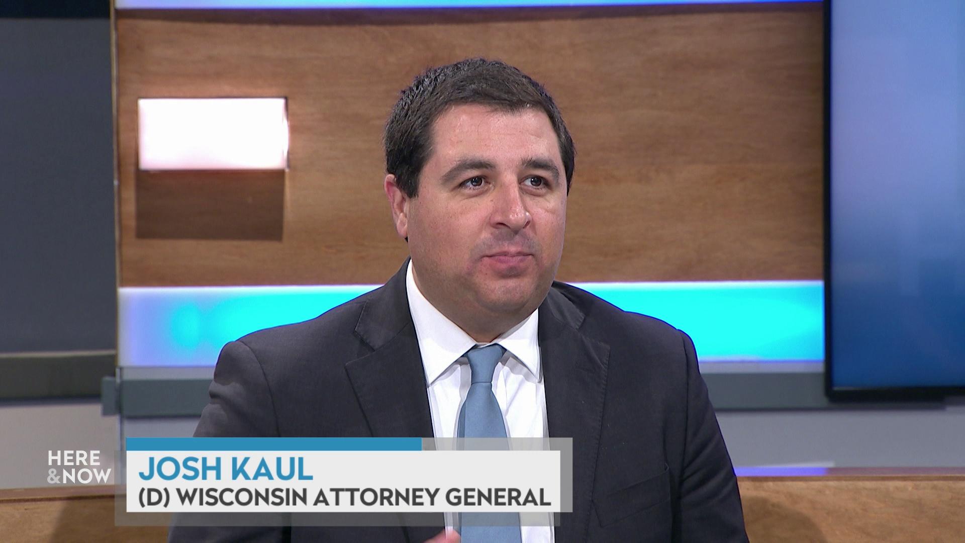 A still image from a video shows Josh Kaul seated at the 'Here & Now' set featuring wood paneling, with a graphic at bottom reading 'Josh Kaul' and '(D) Wisconsin Attorney General.'